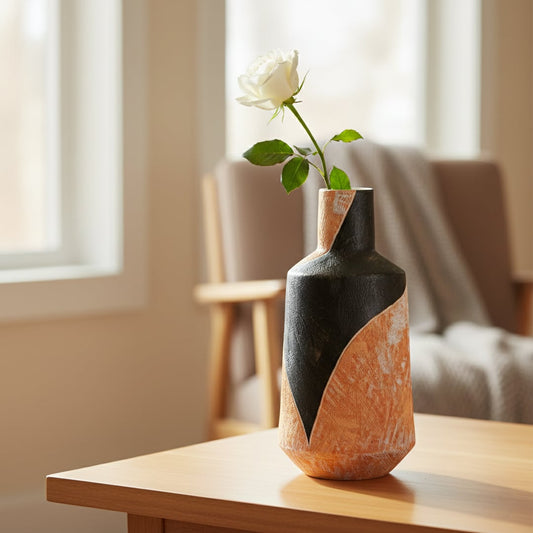 Orange and black textured ceramic decorative vase styled with white rose on wooden side table in warm modern interior.