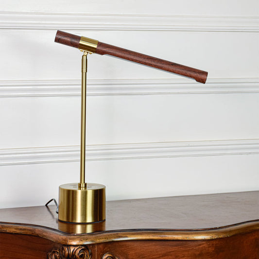 Modern gold metal desk lamp with wooden tube light head and adjustable arm placed on soft off white background.