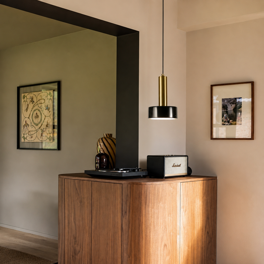 A modern Marshall speaker and a decorative vase sit on a wooden cabinet in a styled interior room with a hanging pendant light and framed wall art.