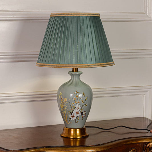 Sage green ceramic table lamp featuring floral detailing gold metal base and pleated fabric shade displayed on white background.