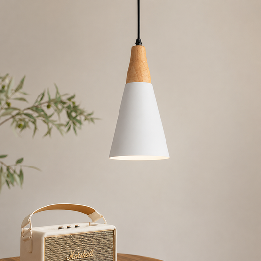 A modern pendant light with a white conical shade and a natural wood cone accent at the top, hanging above a table. A cream-colored Marshall speaker and a blurred green plant are visible in the background against a warm beige wall.