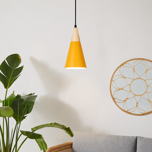 A modern cone-shaped pendant light with a yellow body and a light wood top, hanging in a minimalist room setting next to a green plant and a gray sofa.