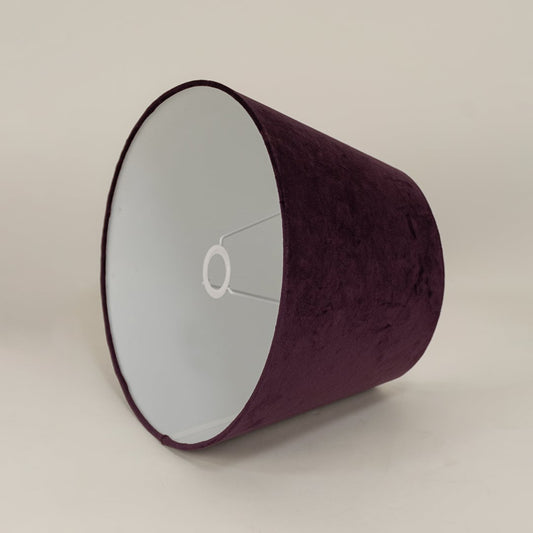 Modern plum velvet lampshade standing against a plain white background capturing its soft surface and simple elegant form.