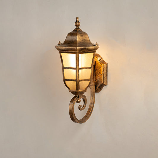 Antique brass outdoor wall lantern on white background with a frosted windowpane shade and an elegant bottom scroll arm.