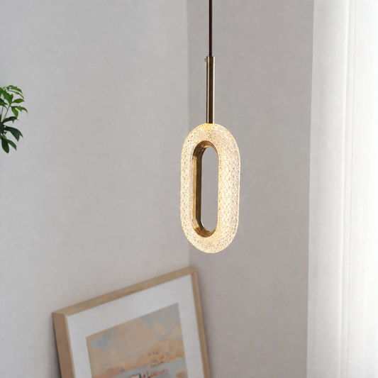 A modern oval pendant light with a textured, woven crackle glass shade and a brushed brass metal frame, hanging in a minimalist room setting.