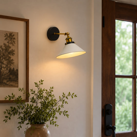 A wall-mounted sconce with a white conical shade, brass-toned hardware, and a black round backplate, lit and mounted on a beige wall next to a wooden door frame.