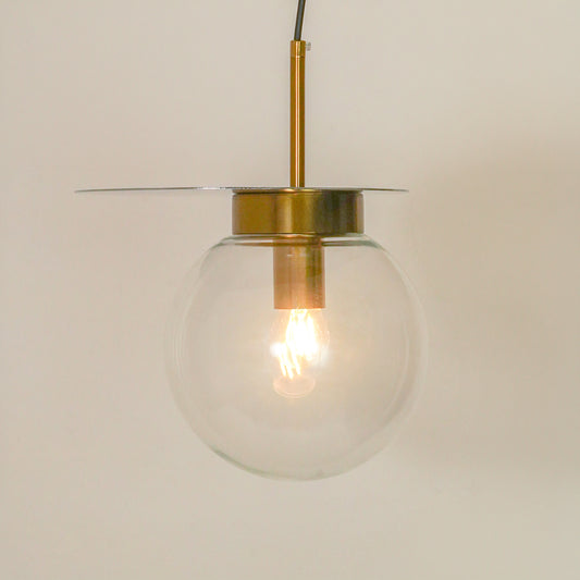 A modern pendant light with a clear glass globe shade, a brass-finished central cap and rod, and a thin horizontal glass disc shade, shown against a plain light beige background.