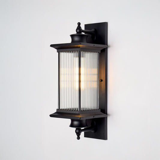 Black aluminum outdoor wall light on white background with linear reeded glass shade and finial trim accents for decor.