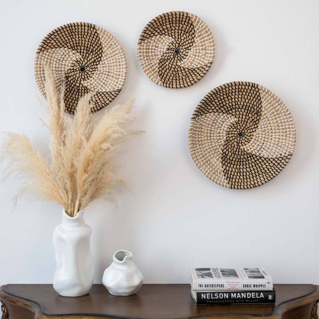 Grouped woven wall baskets styled above wooden console table with white vase for rustic living room wall accent display.