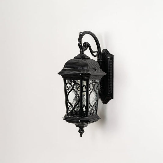 Light off white background displays black metal outdoor wall lantern showcasing ornate design glass texture and sturdy build.