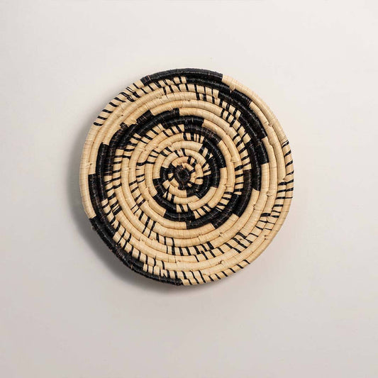 Round handcrafted black and cream woven seagrass wall basket with swirling vortex spiral pattern on white background image.