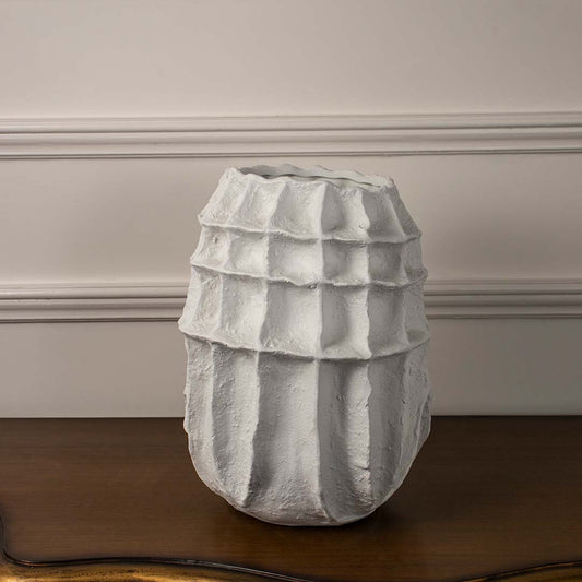 White ceramic vase with geometric layered texture placed on wooden table against neutral wall background for stylish minimal home decor accent.
