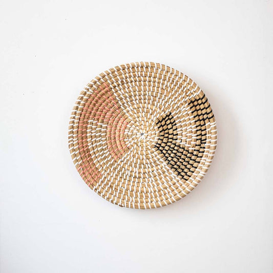 Minimalist woven seagrass wall basket plate featuring geometric orange and black accents isolated on a white backdrop.