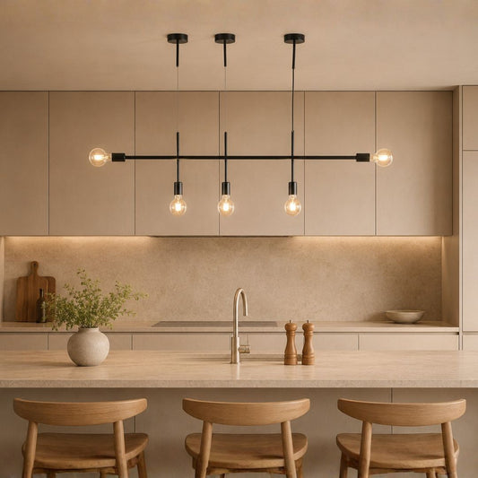 Modern linear pendant light fixture with four exposed bulb lights suspended over a kitchen island in a warm beige interior.