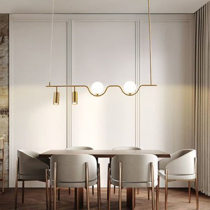 Gold metal linear chandelier with frosted globes and spotlights styled in a modern interior adding warm ambient lighting.