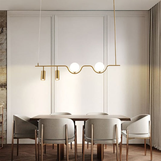 Gold metal linear chandelier with frosted globes and spotlights styled in a modern interior adding warm ambient lighting.