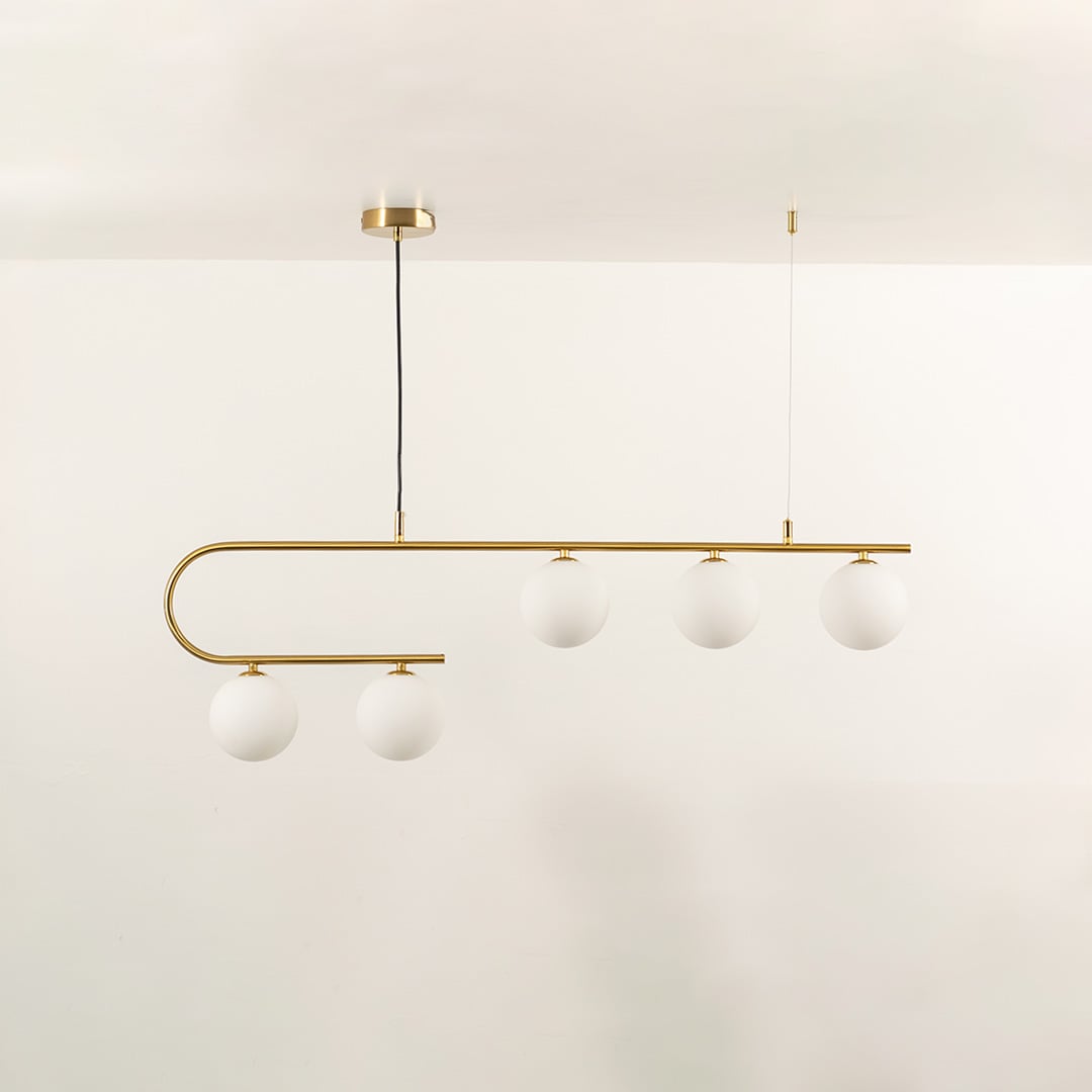 Gold asymmetrical ceiling light with white globes in a front view against a simple wall background with lights on perfect for luxury lighting décor.