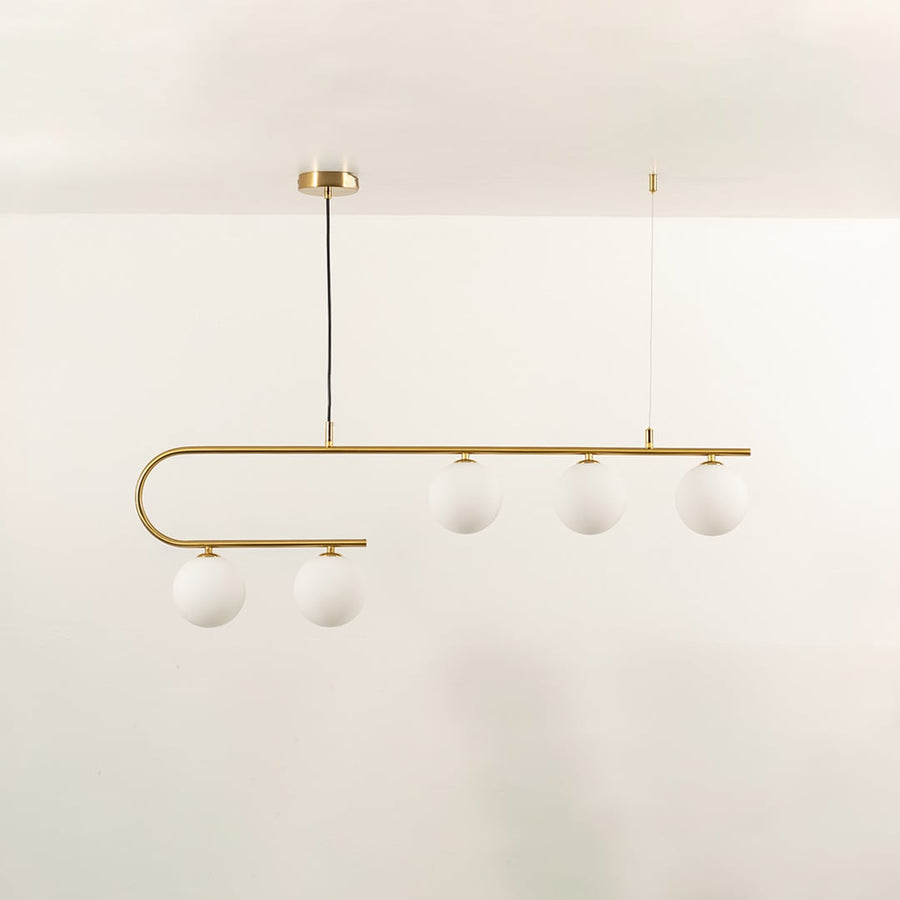 Gold asymmetrical ceiling light with white globes in a front view against a simple wall background with lights on perfect for luxury lighting décor.