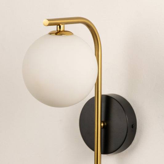 Closeup of modern wall light with frosted glass globe and gold metal arm showing smooth finish and premium design for interior decor.