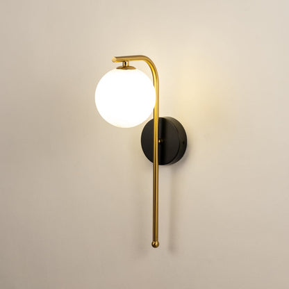 A gold and black metal wall light with a frosted globe shade shown with lights on against a white background highlighting its warm ambient glow.