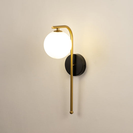 A gold and black metal wall light with a frosted globe shade shown with lights on against a white background highlighting its warm ambient glow.
