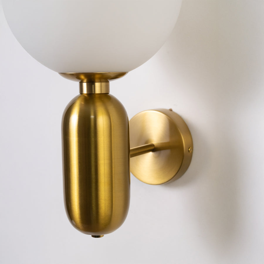 Elegant gold metal wall sconce with smooth cylindrical body fixed on clean white wall background perfect for luxury interior decor lighting.