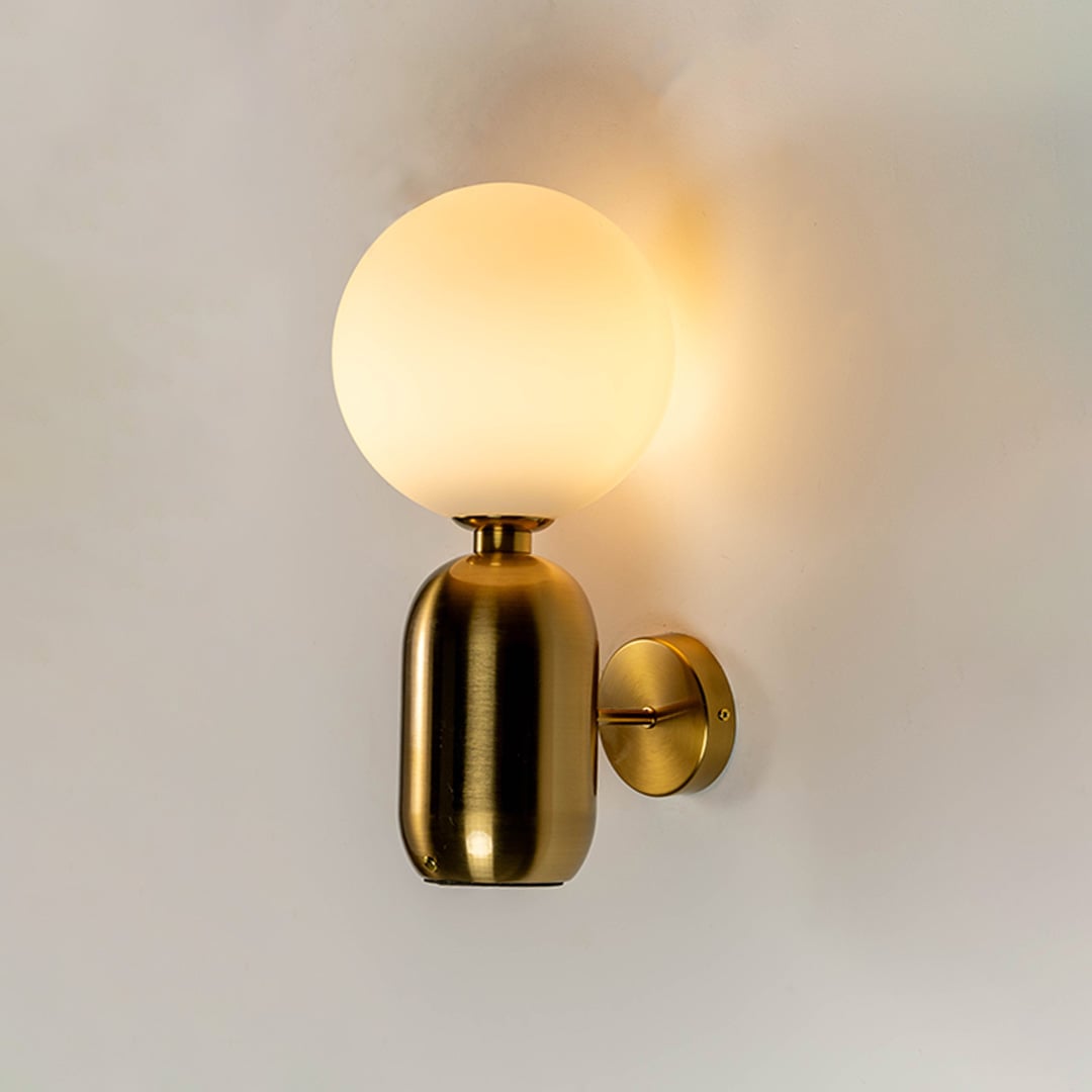 Luxury brass wall sconce with frosted glass globe shade glowing warm light white background for bedroom hallway and modern home decor.