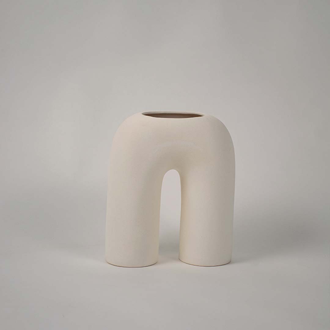Matte cream ceramic arch vase displayed on a plain white background highlighting its sculptural form for minimal home decor accents.