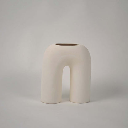 Matte cream ceramic arch vase displayed on a plain white background highlighting its sculptural form for minimal home decor accents.