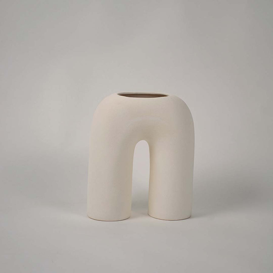 Matte cream ceramic arch vase displayed on a plain white background highlighting its sculptural form for minimal home decor accents.