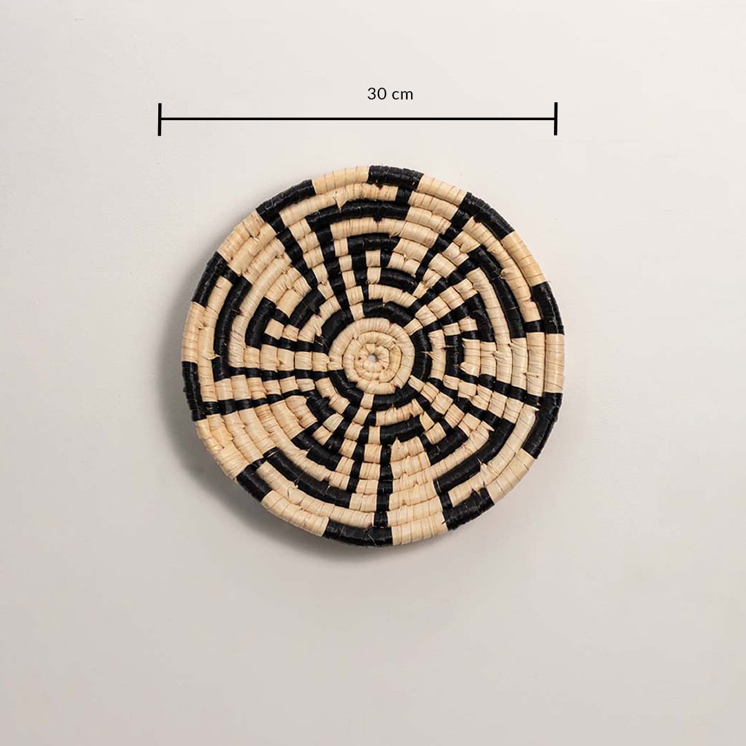 A handwoven natural and black rattan wall decor plate displayed on a white background clearly showing a diameter of 30 cm for accurate wall decor measurement.
