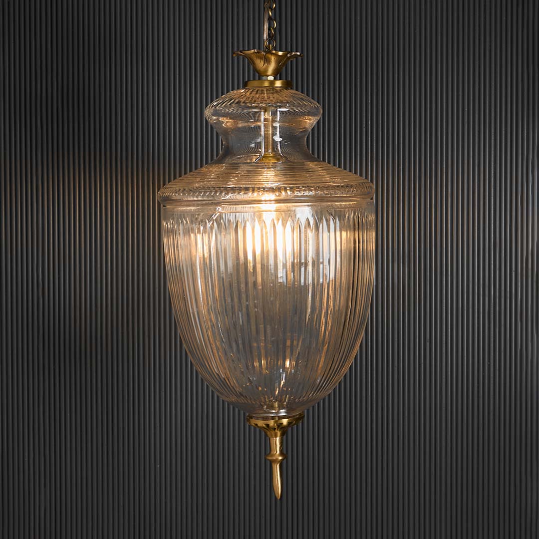 Clear glass lantern pendant light with brass accents glowing for luxurious interiors.