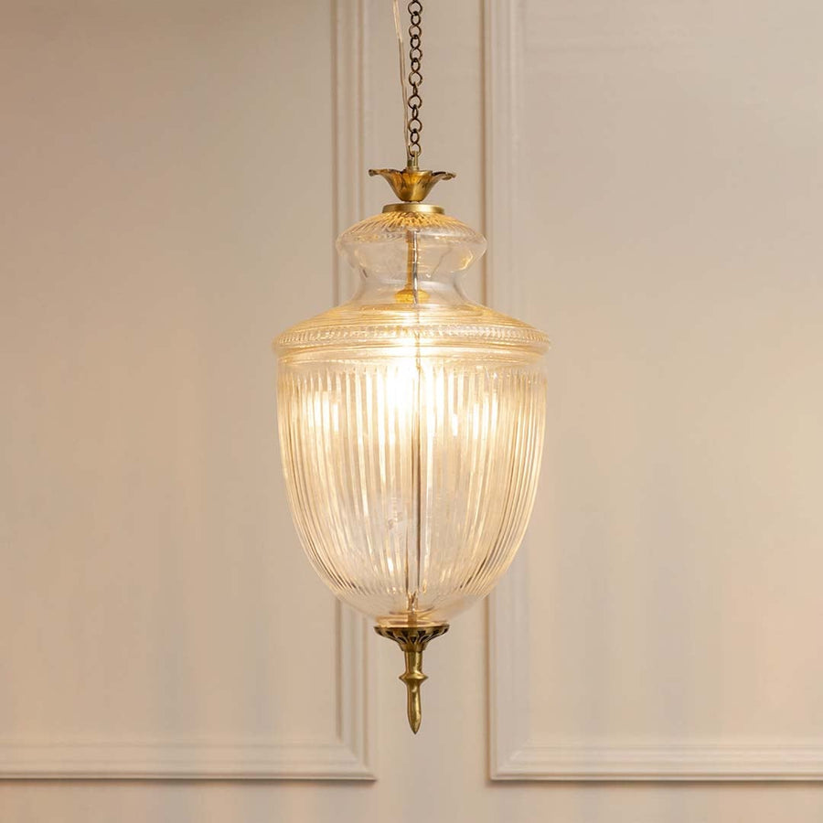 Antique brass and ribbed glass lantern pendant light with warm glow for refined home decor spaces.