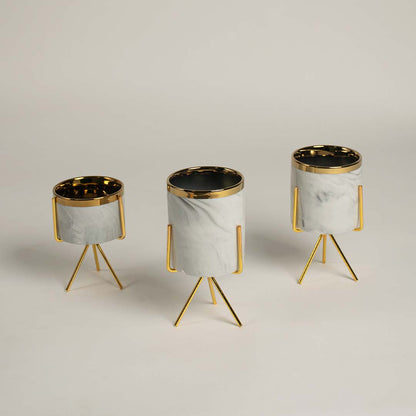 A white marble finish planter with a gold metal stand placed on a bright surface highlighting its sleek modern shape and elegant style.