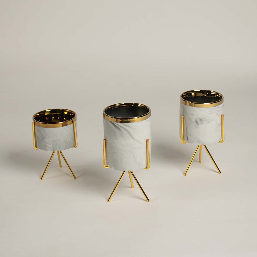 A white marble finish planter with a gold metal stand placed on a bright surface highlighting its sleek modern shape and elegant style.