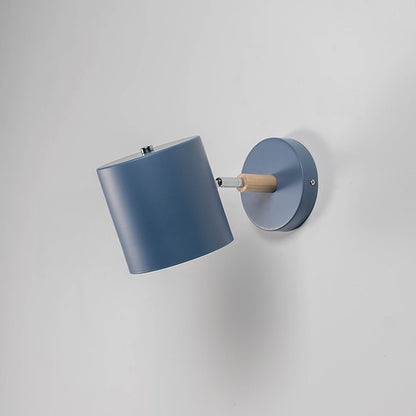 A blue wall lamp with light off is set against a grey background showcasing its matte blue shade round base and wooden connector with a strong modern silhouette.
