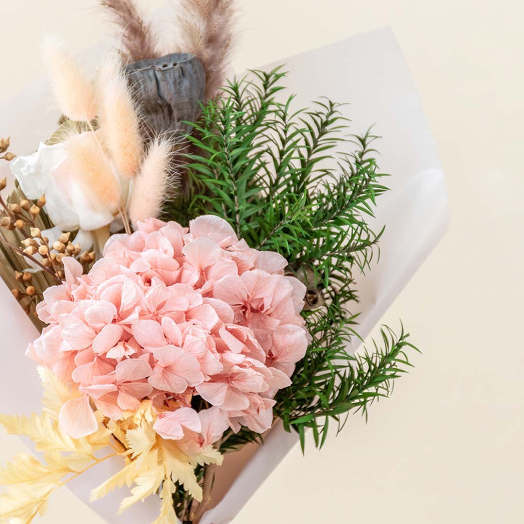 Closeup of a soft pink preserved hydrangea bouquet mixed with green pine foliage and bunny tails for cozy winter gifting.