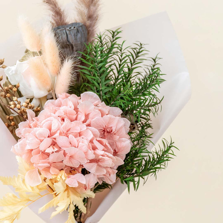 Closeup of a soft pink preserved hydrangea bouquet mixed with green pine foliage and bunny tails for cozy winter gifting.