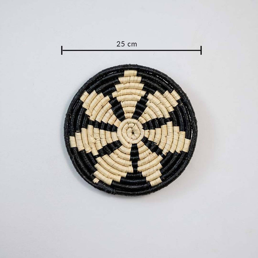 Round woven coaster with black and beige pattern on a white background, with a measurement label indicating 25 cm.
