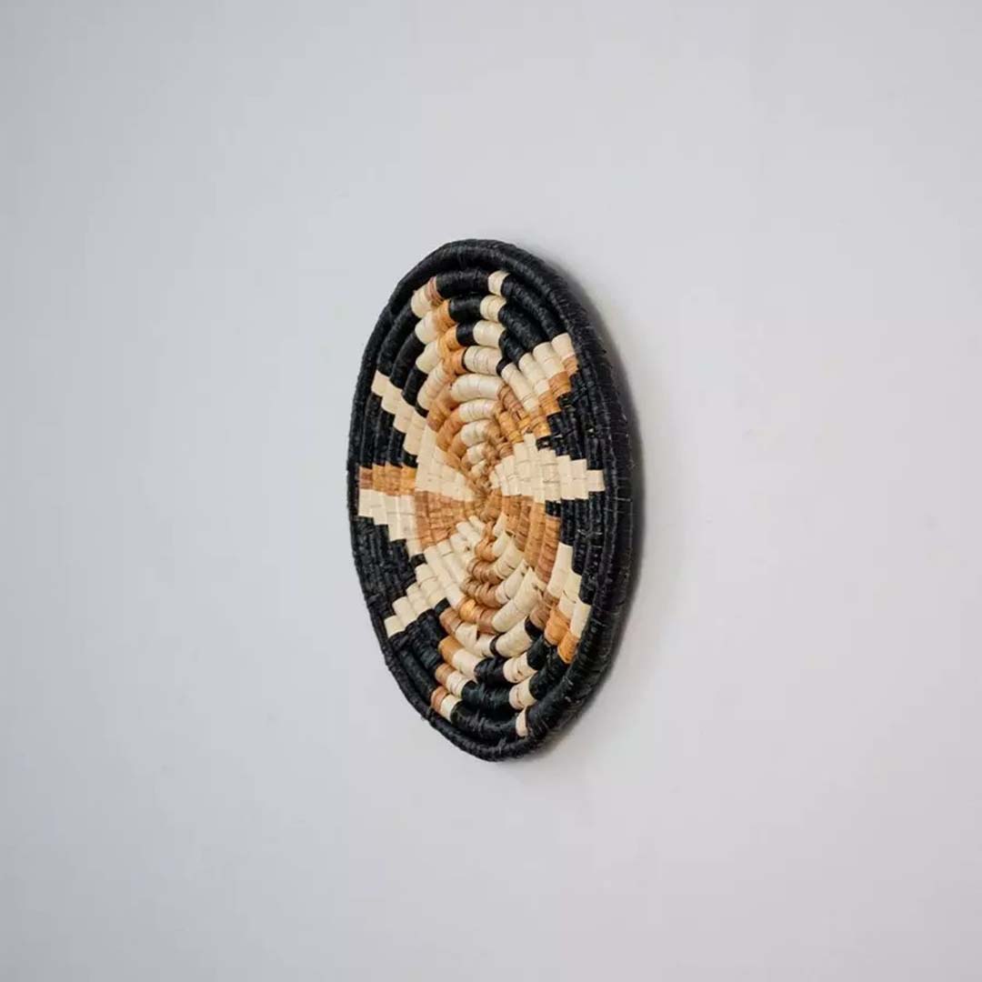 Side angle of handwoven bamboo wall plate in black beige tones highlighting natural texture and crafted finish.