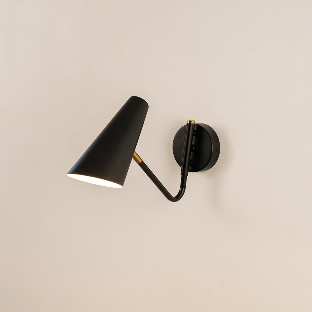 Black cone wall light with brass accents glowing softly on white wall offering modern elegance and ambient lighting style.