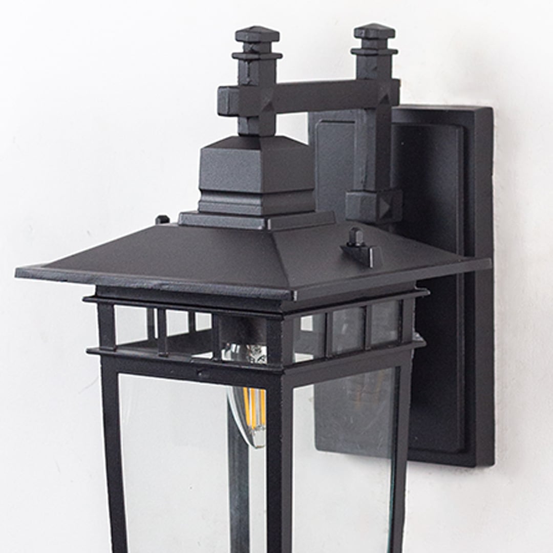 Closeup of outdoor wall lantern light with black frame clear glass and glowing bulb for modern home exteriors.