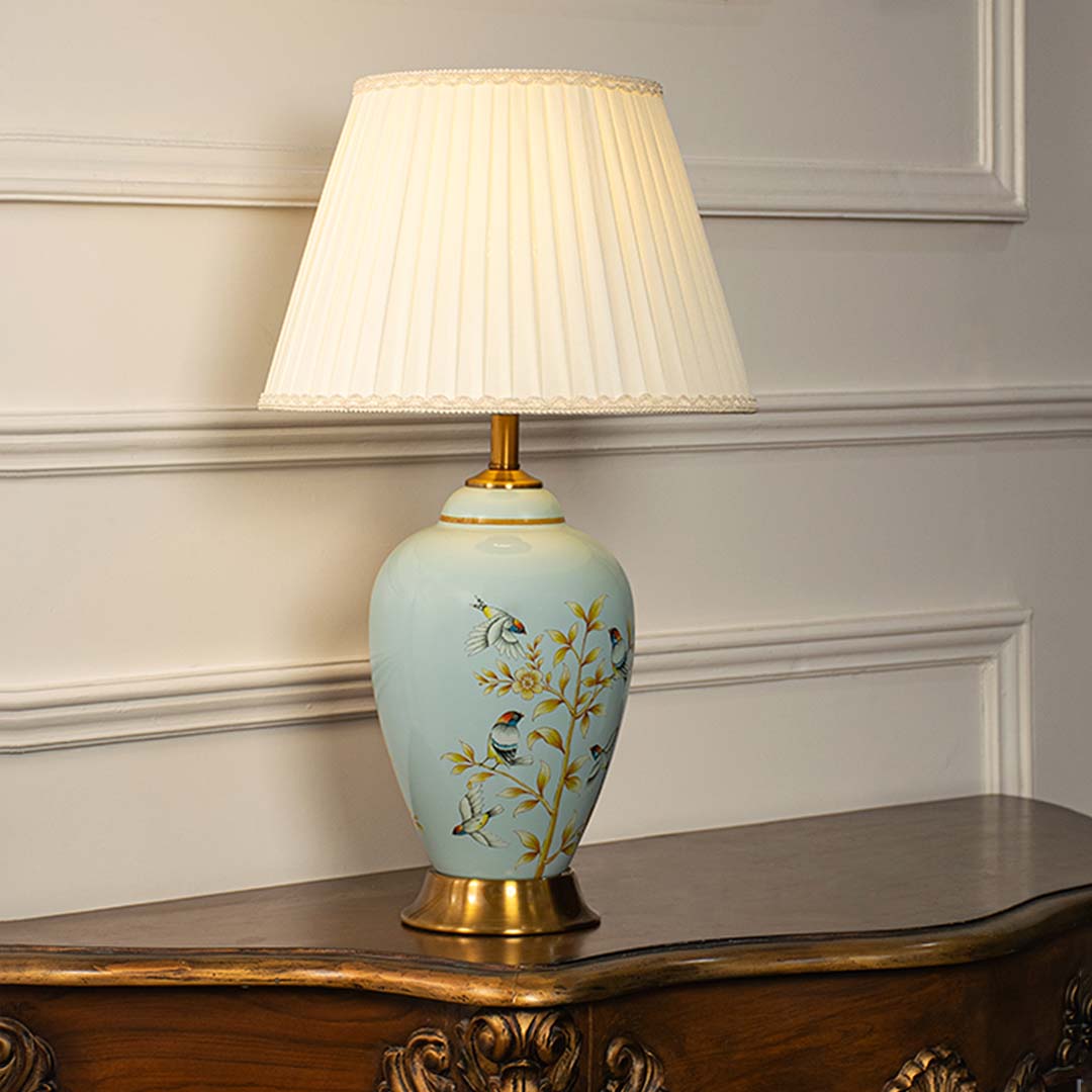 Ceramic table lamp with pleated shade light on white background blue floral and bird painted base with golden decorative stand.