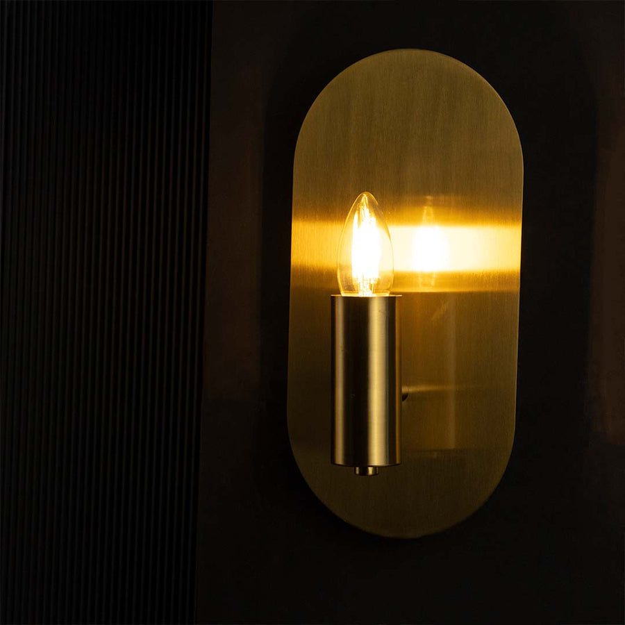 Golden wall sconce glowing softly on black background highlighting warm light and luxurious metallic texture.