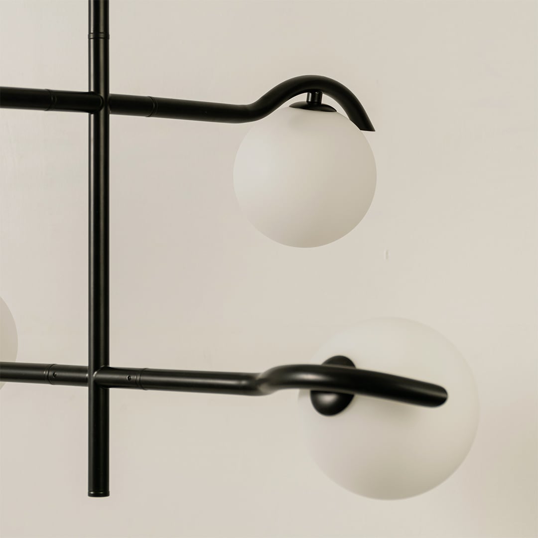 Closeup view of black metal chandelier showing curved metal arms and matte white globes for stylish modern interior lighting.
