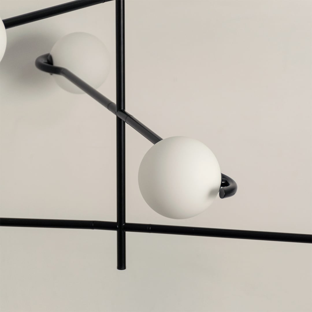 Closeup of black metal chandelier showing curved arms and matte white globes for stylish contemporary interior lighting.