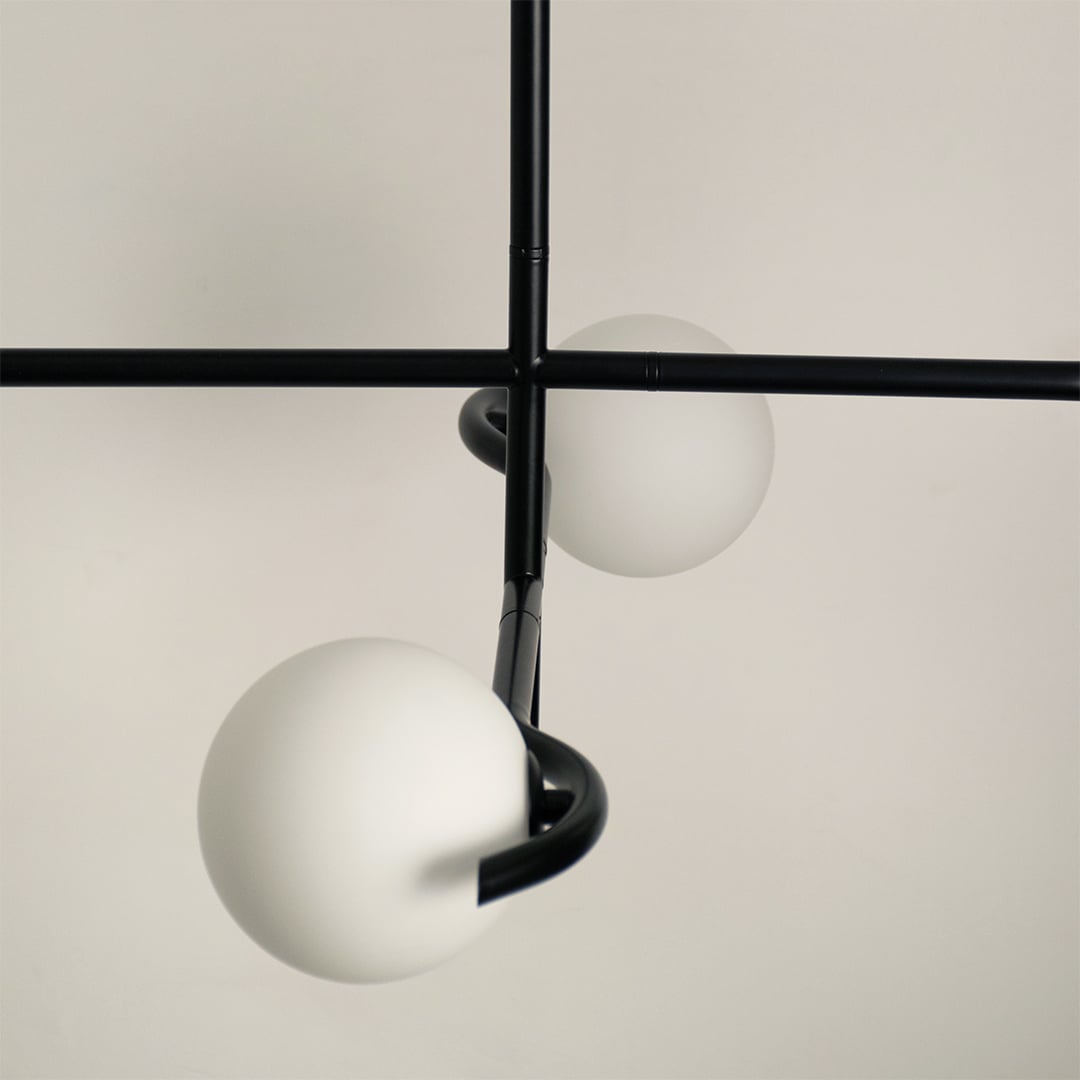 Detailed closeup of black metal chandelier highlighting crossed arms and soft matte white globes for elegant modern decor.