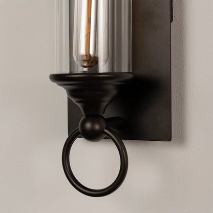 Closeup of black metal wall sconce highlighting clear glass tube and ring accents for a refined outdoor lighting look.