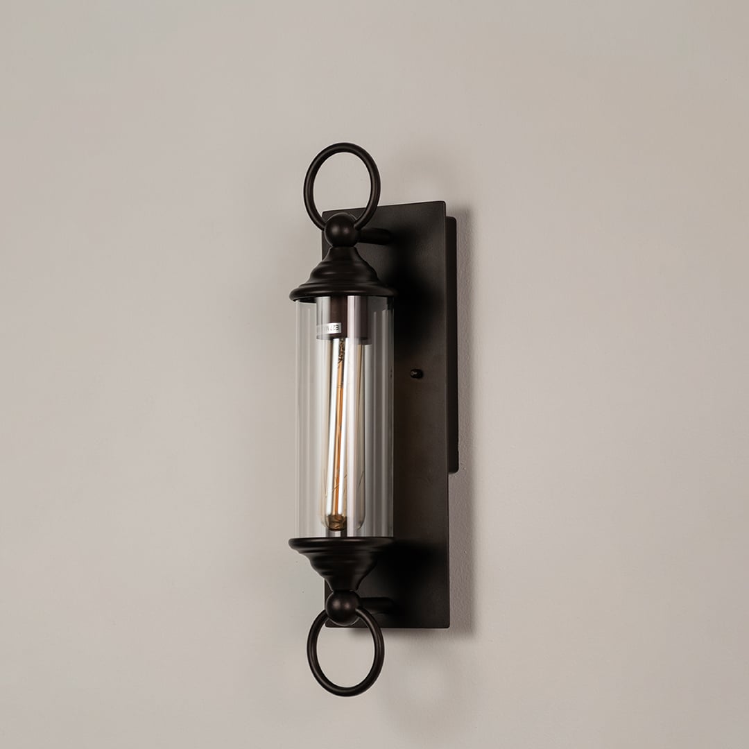 Black metal wall sconce with clear glass tube and ring accents shown on white background for elegant outdoor decor appeal.