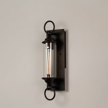 Black metal wall sconce with clear glass tube and ring accents shown on white background for elegant outdoor decor appeal.
